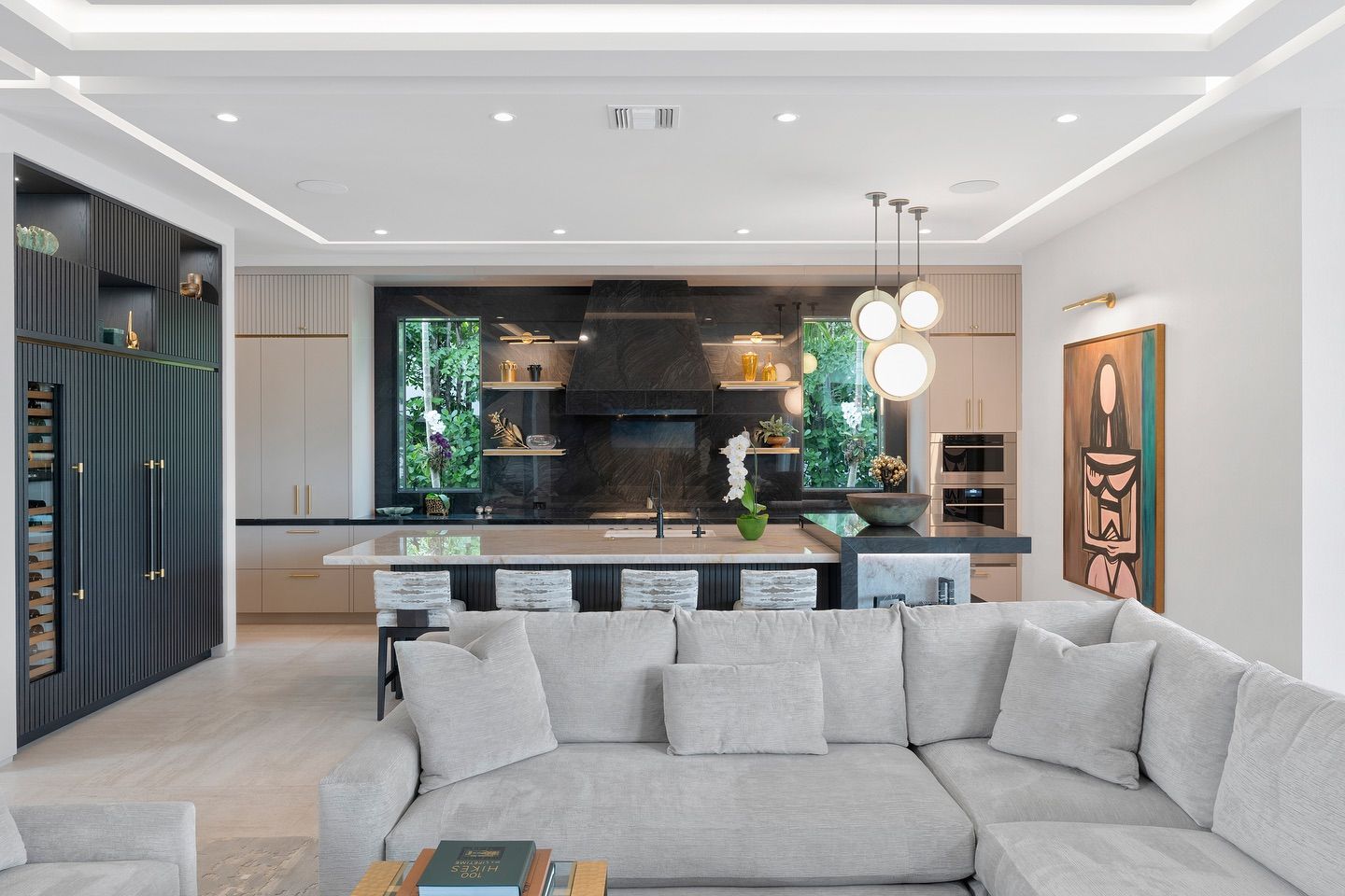 Modern kitchen with a light-colored sectional sofa. Includes a kitchen island, black cabinetry, and hanging globe lights.