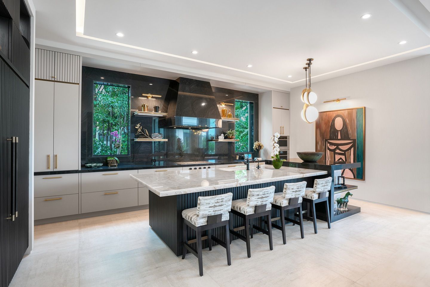 Modern kitchen with island seating, black and white design, marble countertop, and artwork.