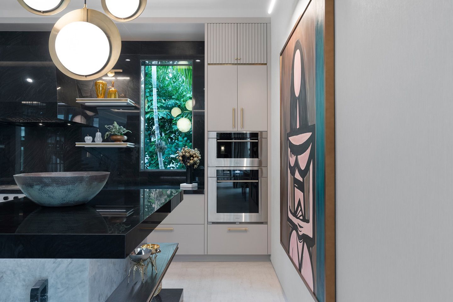 Modern kitchen with black countertops, light cabinets, built-in oven, and a large abstract painting.