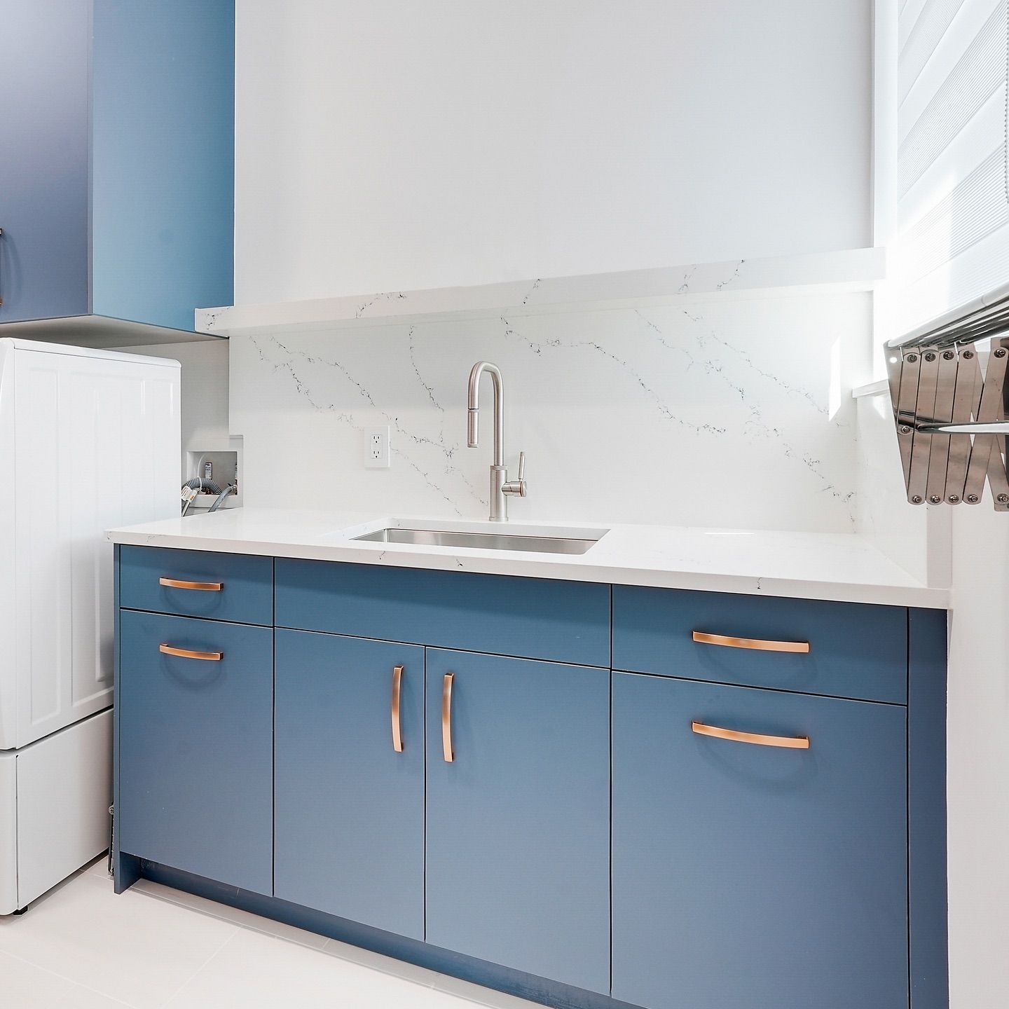 Blue laundry room cabinet with a sink, white countertop, and copper hardware.