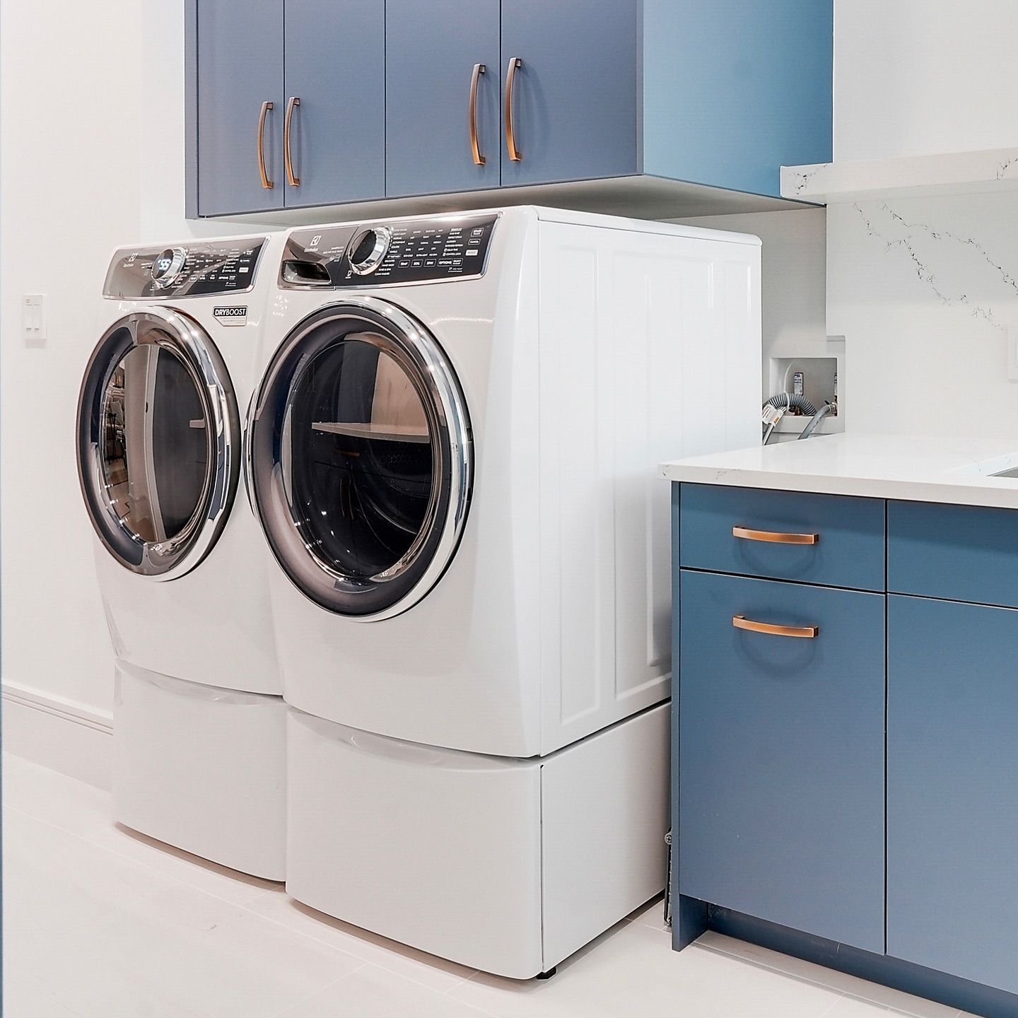 A white washing machine and dryer sit in a blue laundry room with cabinets and countertops.