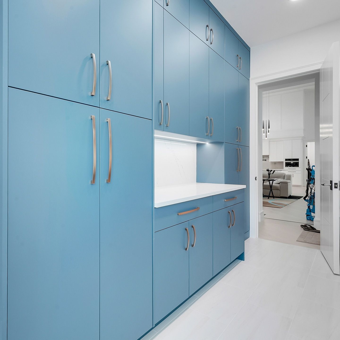 Blue cabinets with silver handles in a laundry room, with a white countertop and a hallway view.