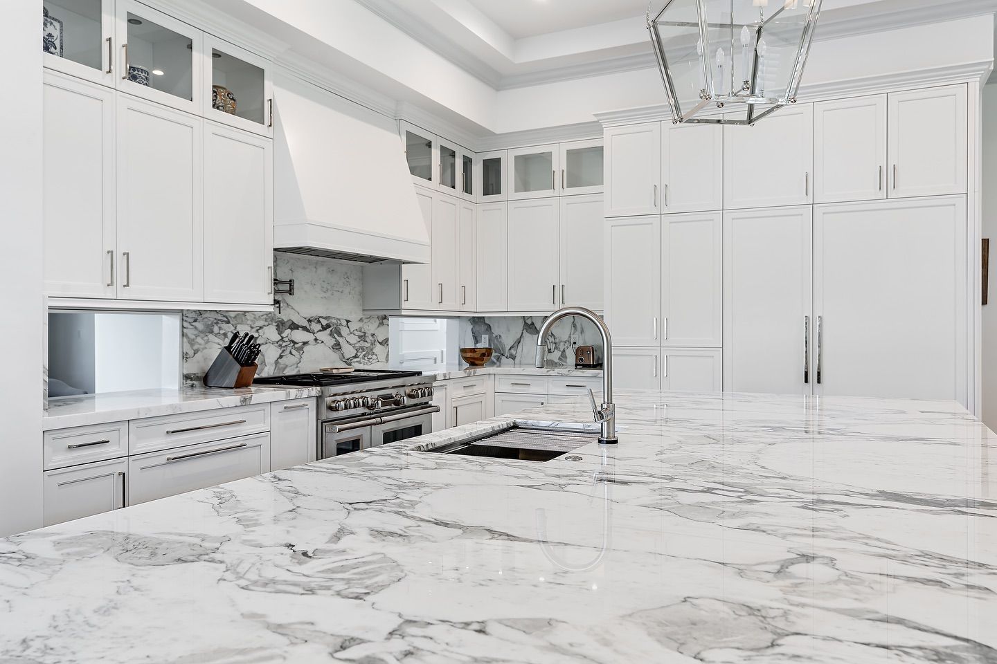 White kitchen with marble countertops and cabinets, stainless steel appliances, and a hanging light.