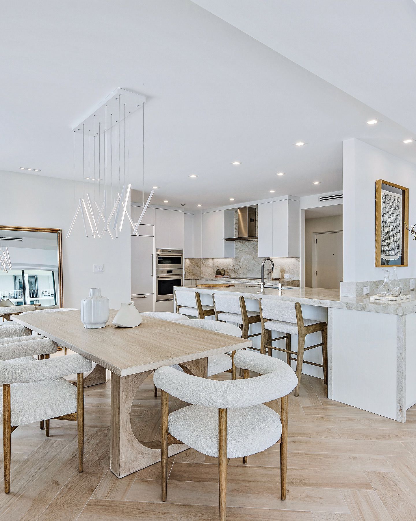Modern, white kitchen and dining area with light wood table and fluffy chairs.