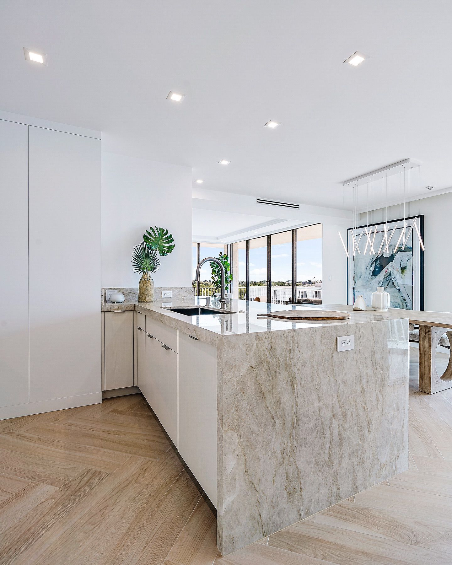 Modern kitchen with light wood floor and granite island. White cabinets, large window with water view.
