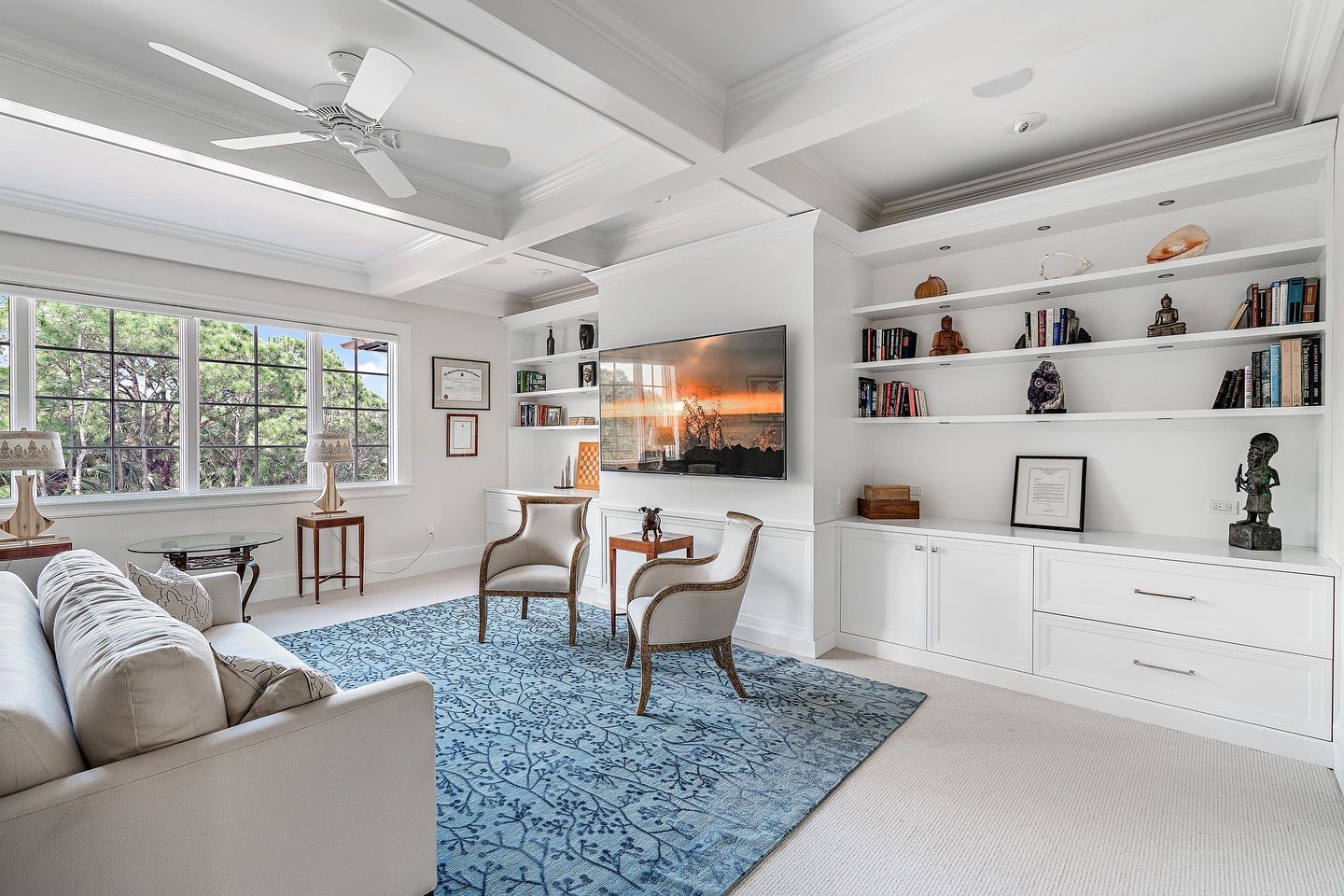 Living room with white built-ins, blue rug, and large window. Two chairs face TV.