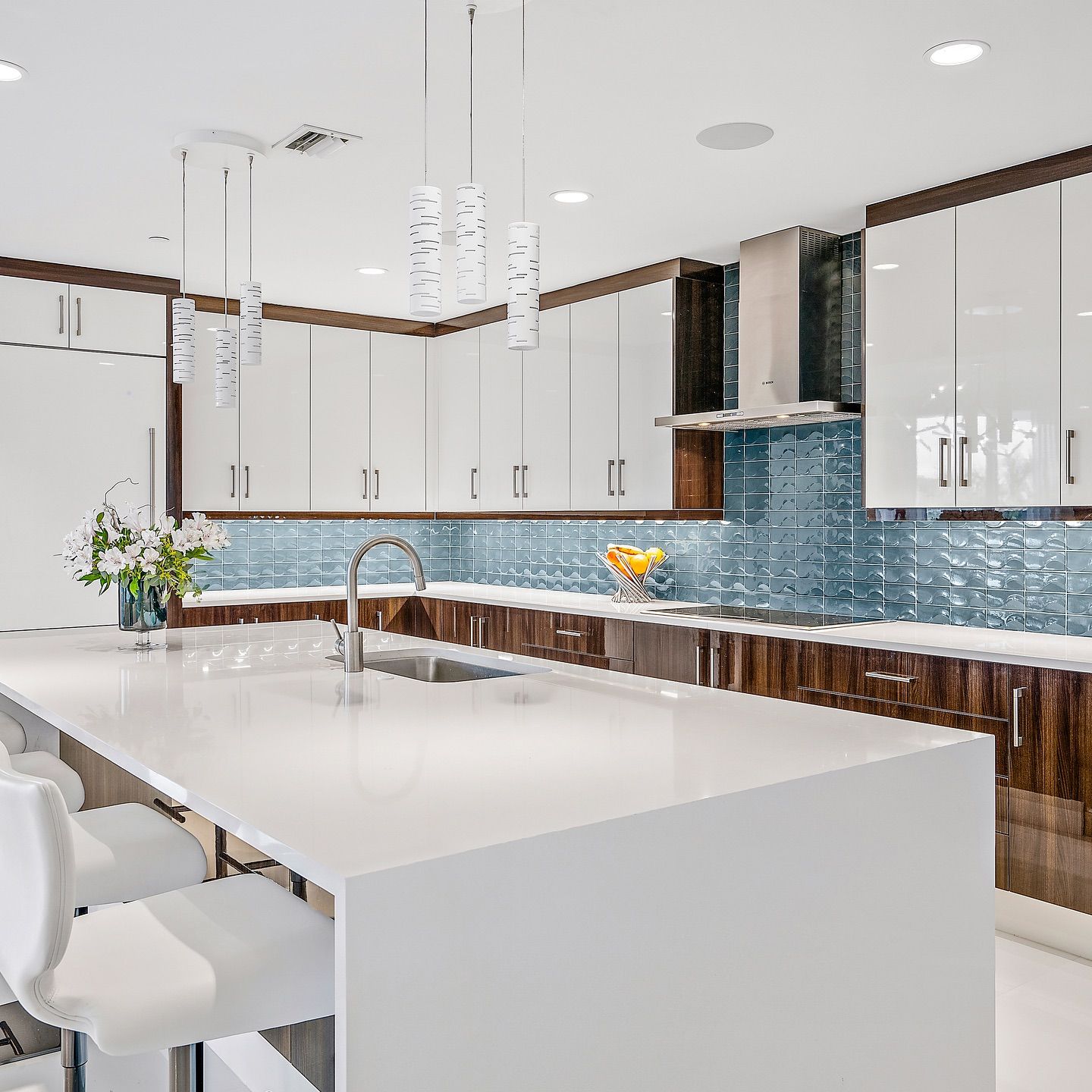 Modern kitchen with white countertops, glossy white cabinets, wood accents, and blue tile backsplash.