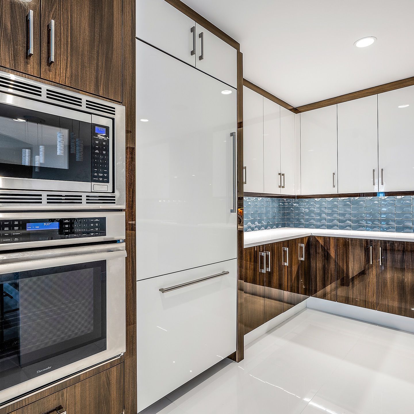 Modern kitchen with white and wood cabinetry, stainless steel appliances, and blue tile backsplash.