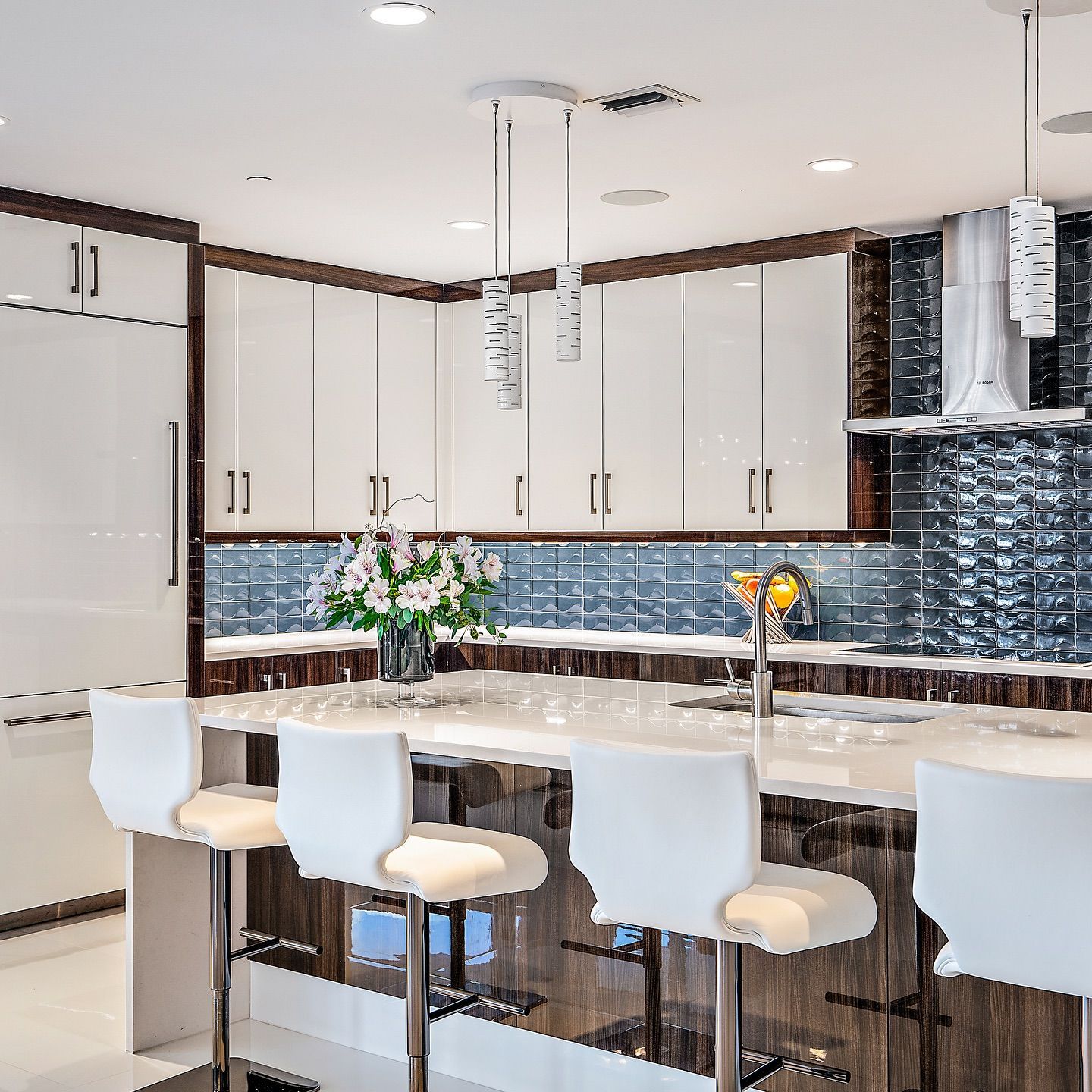 Modern kitchen with white cabinets, dark wood trim, and a marble countertop. White bar stools and pendant lights.