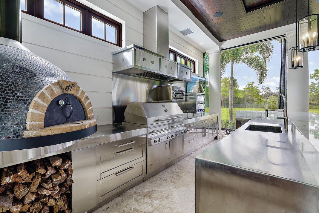 Outdoor kitchen with pizza oven, grill, stainless steel counters, and view of a yard.