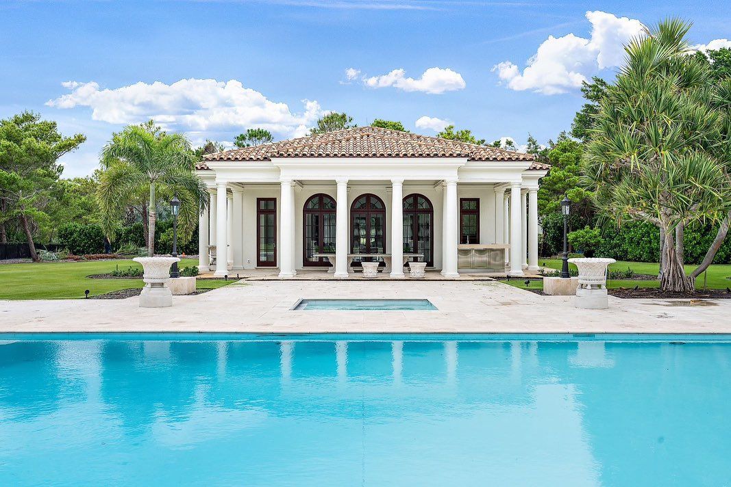 White villa with columns, overlooking a turquoise pool, under a blue sky.