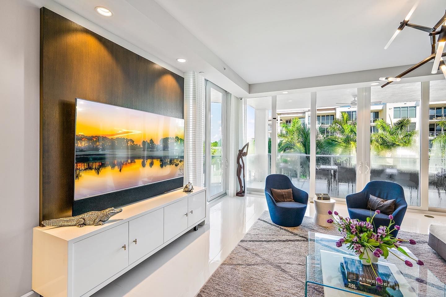 Modern living room with TV mounted on wall, overlooking a balcony and two blue armchairs.