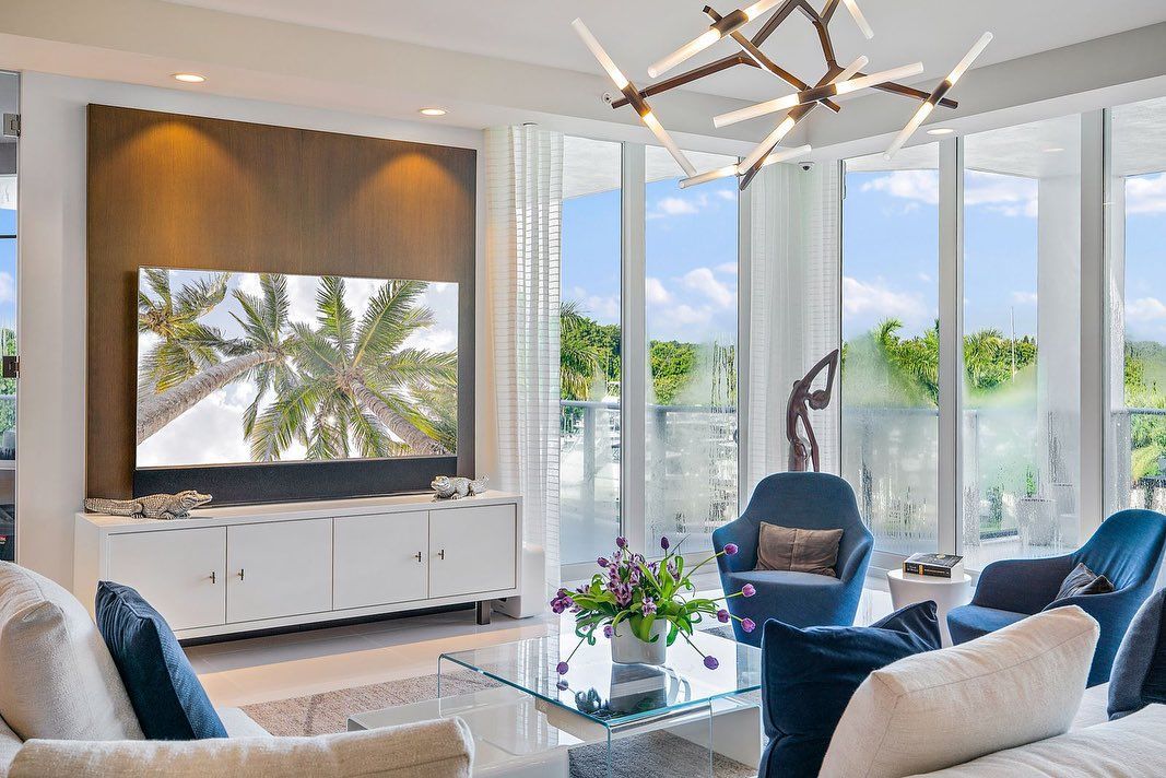 Living room with blue accents, large windows, TV, and modern chandelier.