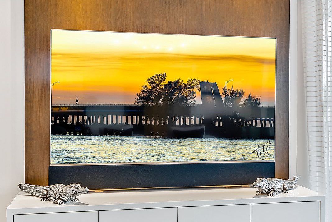 Sunset over a pier, with a golden sky and silhouetted buildings reflected in the water.