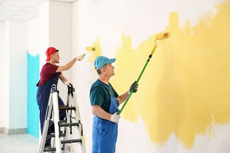 Two men are painting a wall with paint rollers.