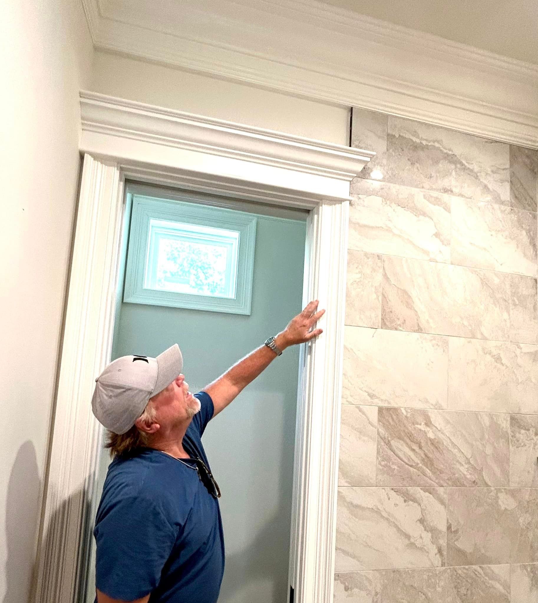 a man in a baseball cap is pointing up at the ceiling in a bathroom .