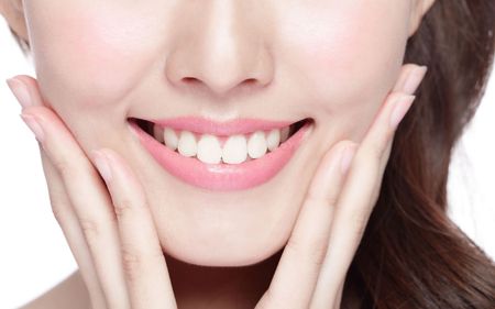 A woman is smiling and touching her face with her hands.
