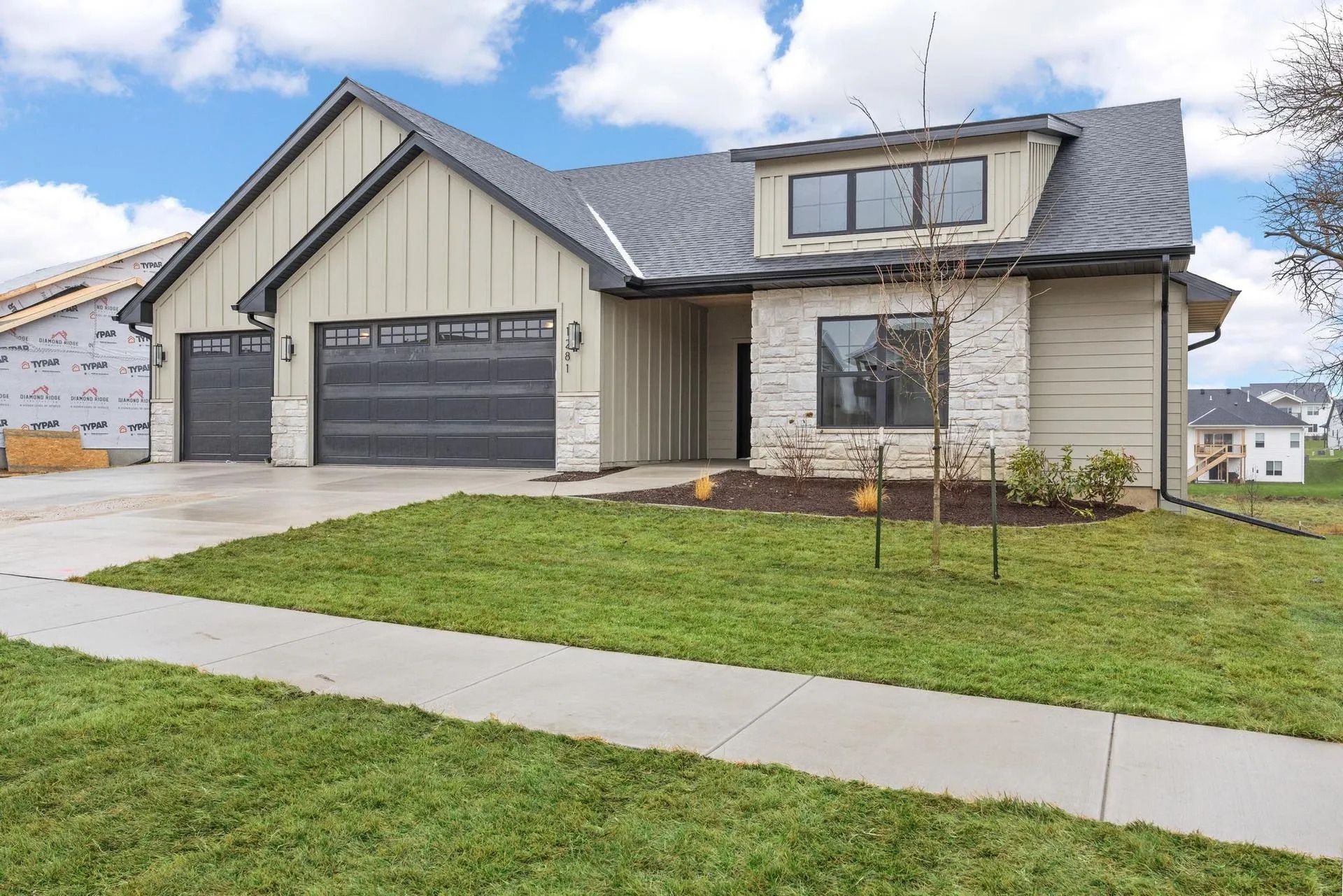 Suburban house with gray siding, dark garage doors, and a front lawn under a cloudy sky