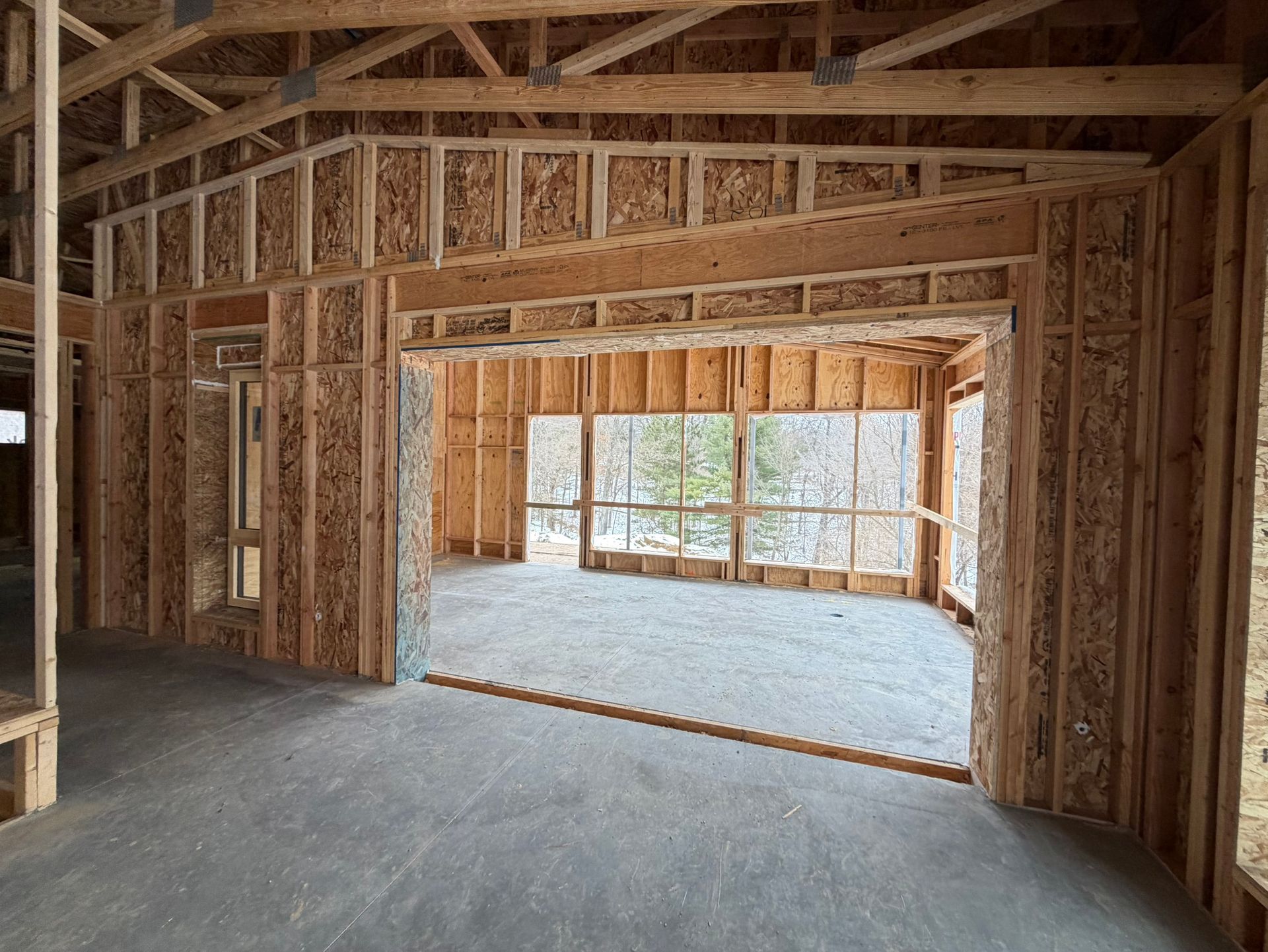 Unfinished wooden house interior with exposed framing and a large opening to a bright windowed room