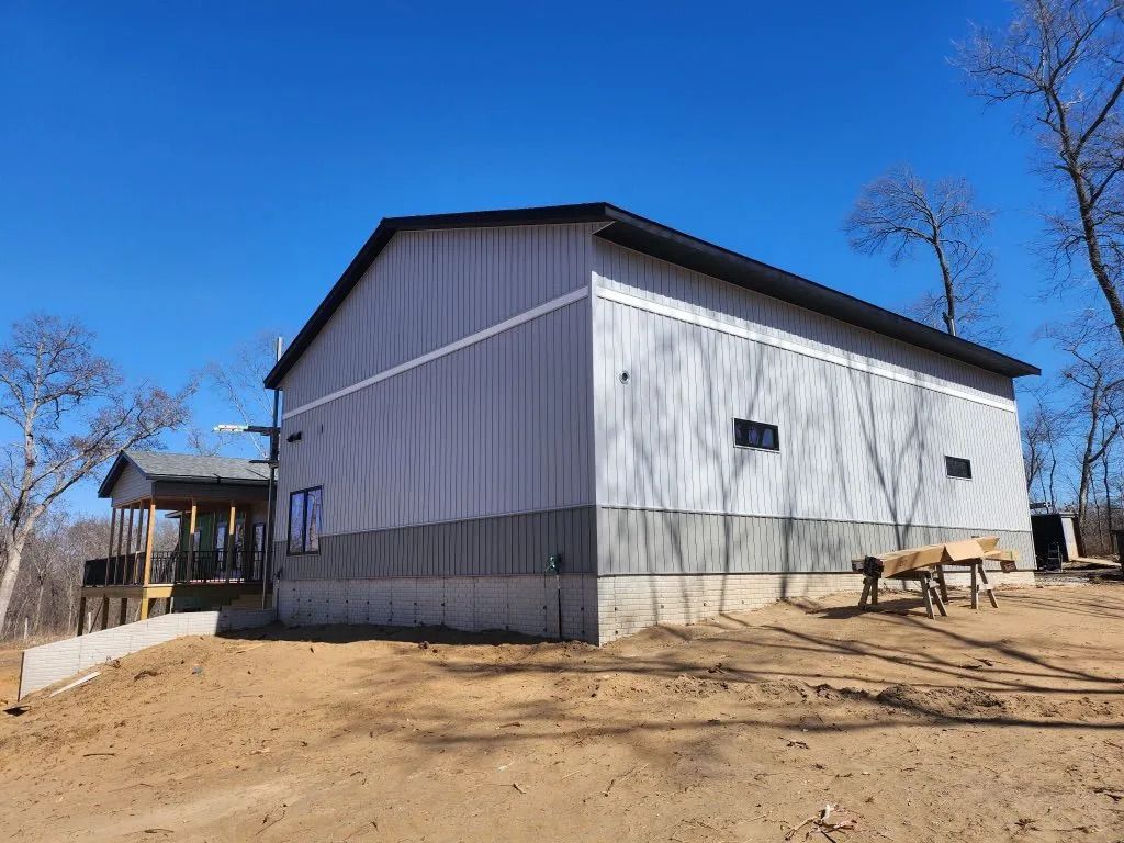 Large gray barn or warehouse on a dirt lot under a clear blue sky