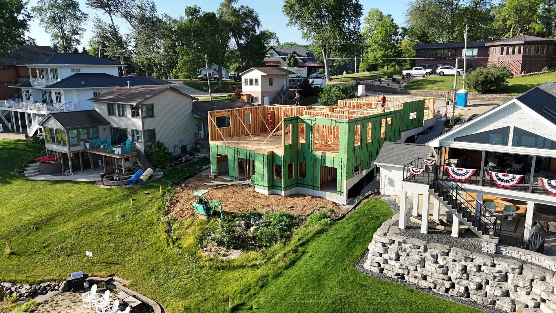 Several houses under construction on a sunny hillside with green grass and trees