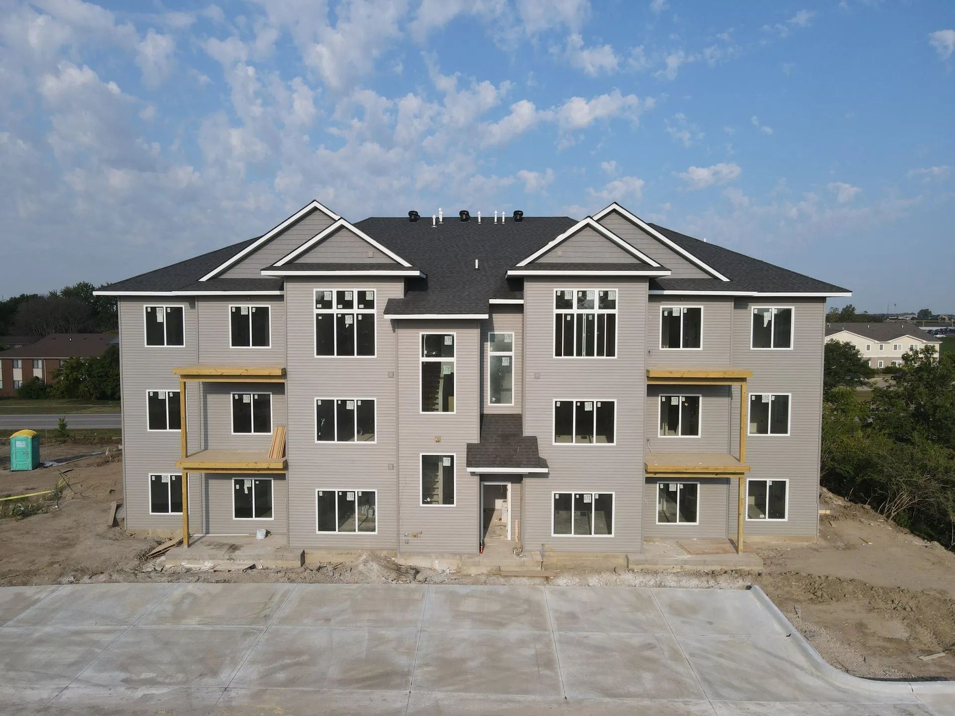 New apartment building under construction with beige siding and gray roof under a cloudy sky