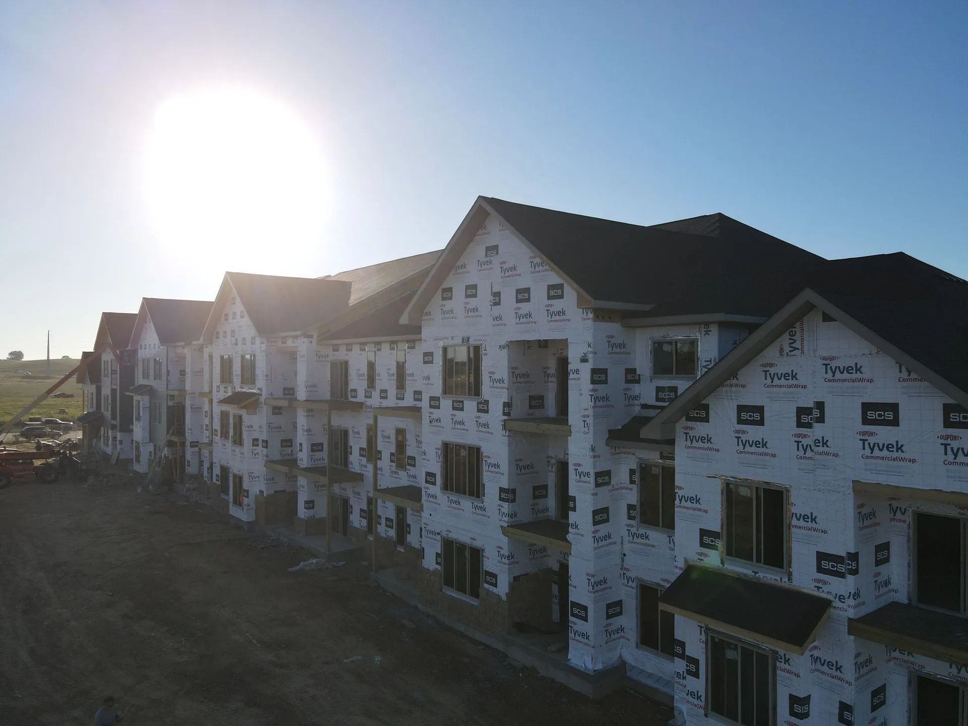 Sunlit row of white apartment buildings under construction at dawn or dusk.