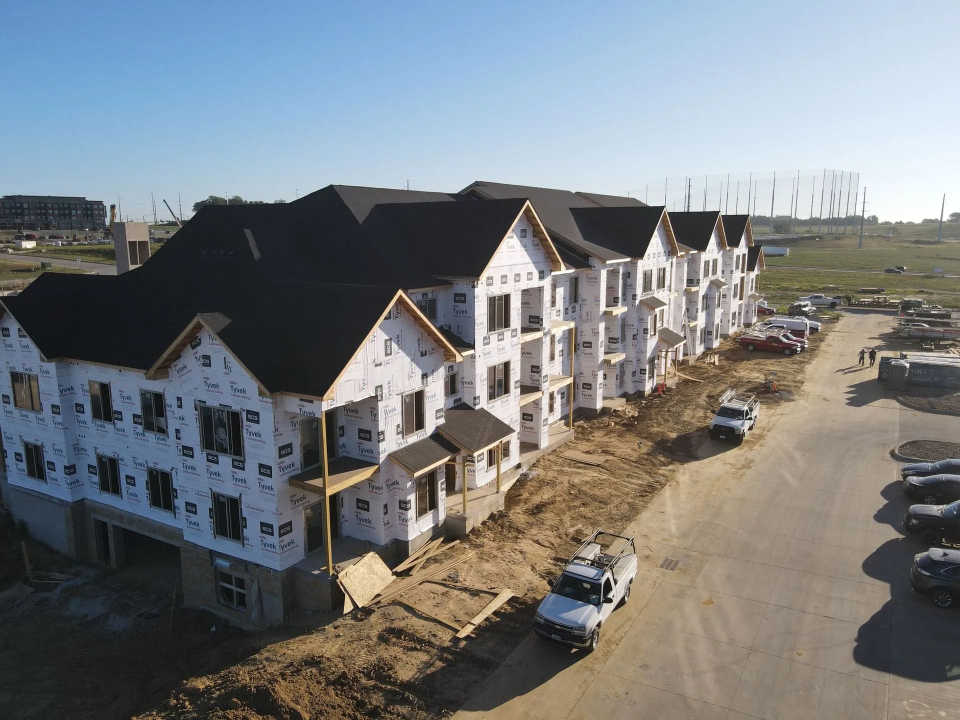 Partially built white townhouses with black roofs along a dirt road under construction