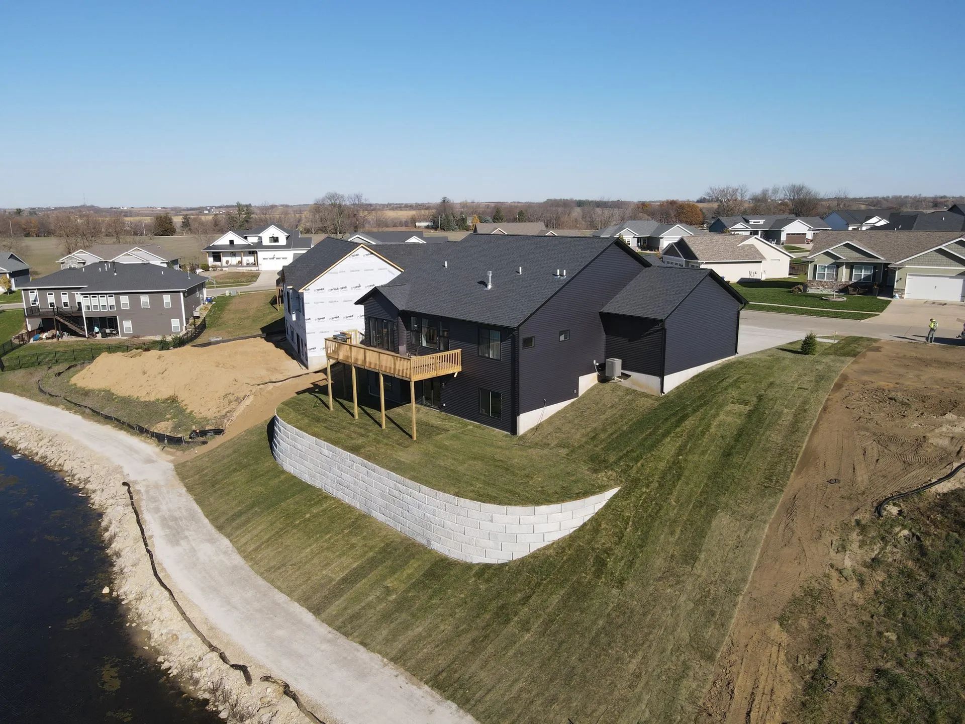 New suburban house with dark roof and deck on a grassy hill under a clear sky