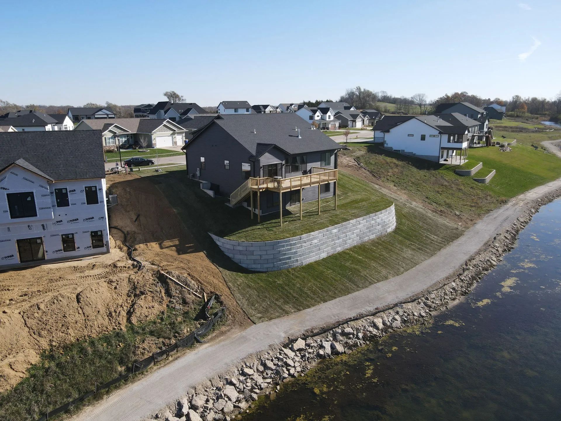 Aerial view of a new house on a grassy lot beside a curving stone-lined road in a residential area