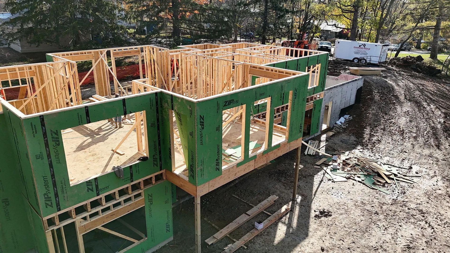 Partially built house with green insulated walls and exposed framing at a muddy construction site