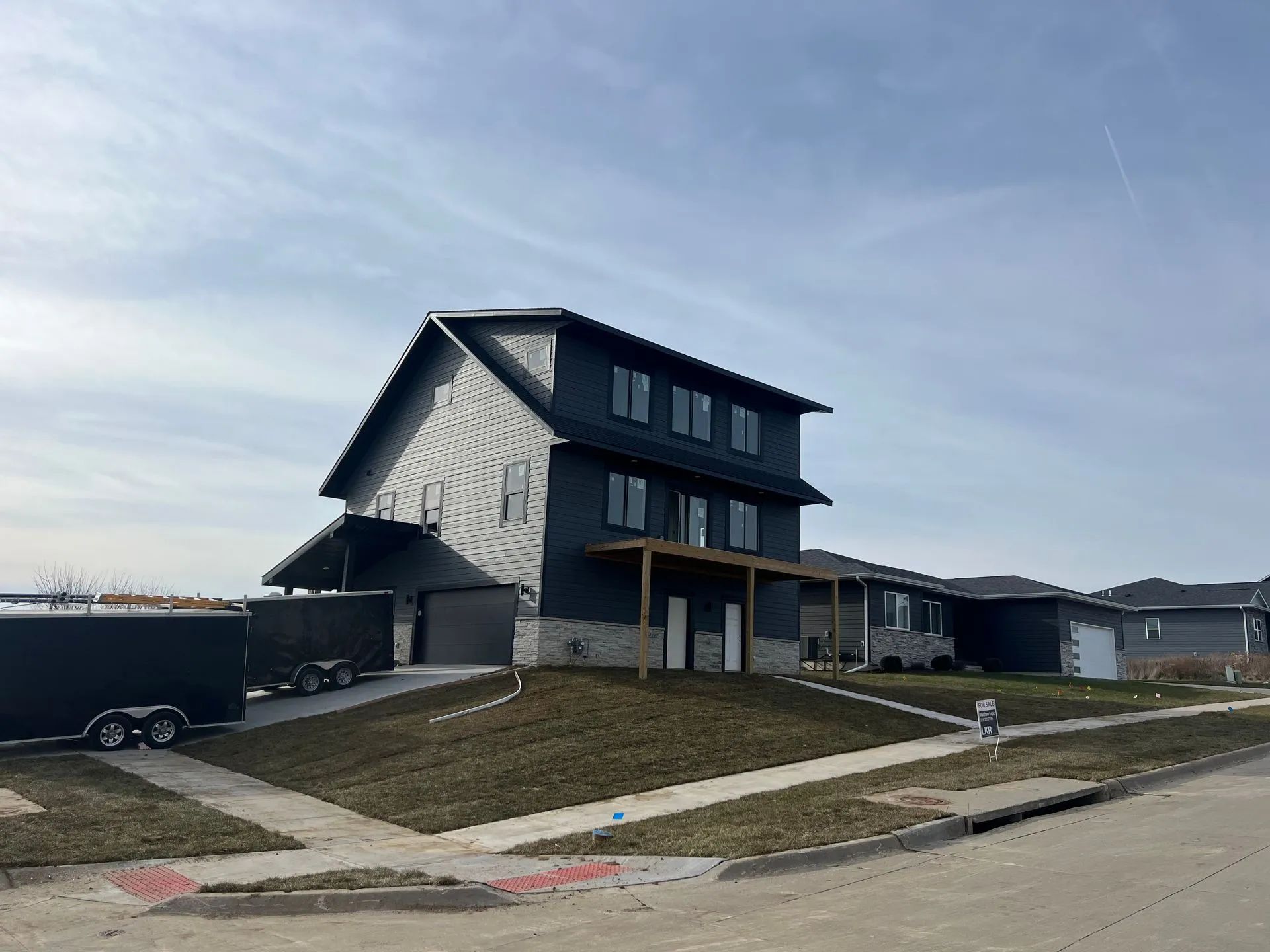 Modern gray house on a corner lot with a sloped lawn and overcast sky.