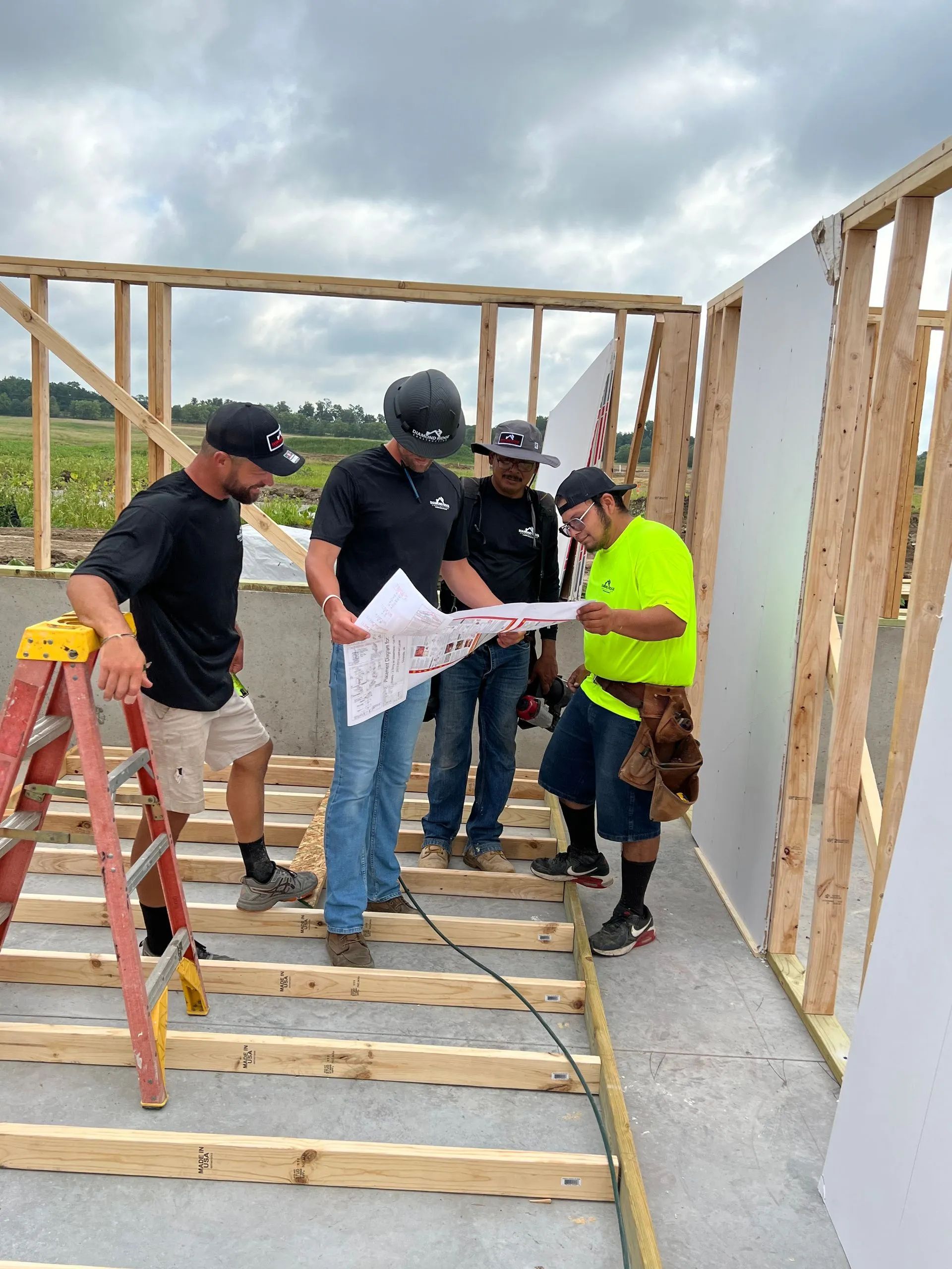 Workers reviewing plans inside a house frame on a construction site, one in a neon safety shirt.