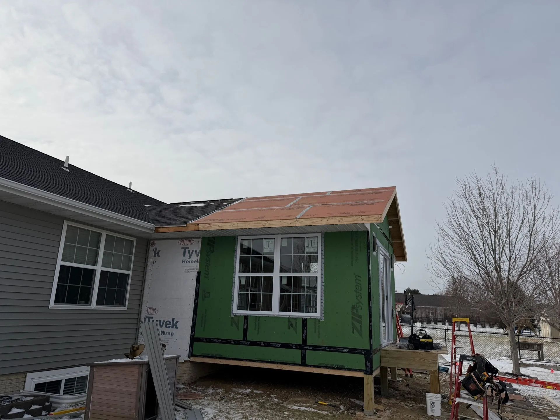 House under construction with green exterior siding and a partially finished roof beside a gray building
