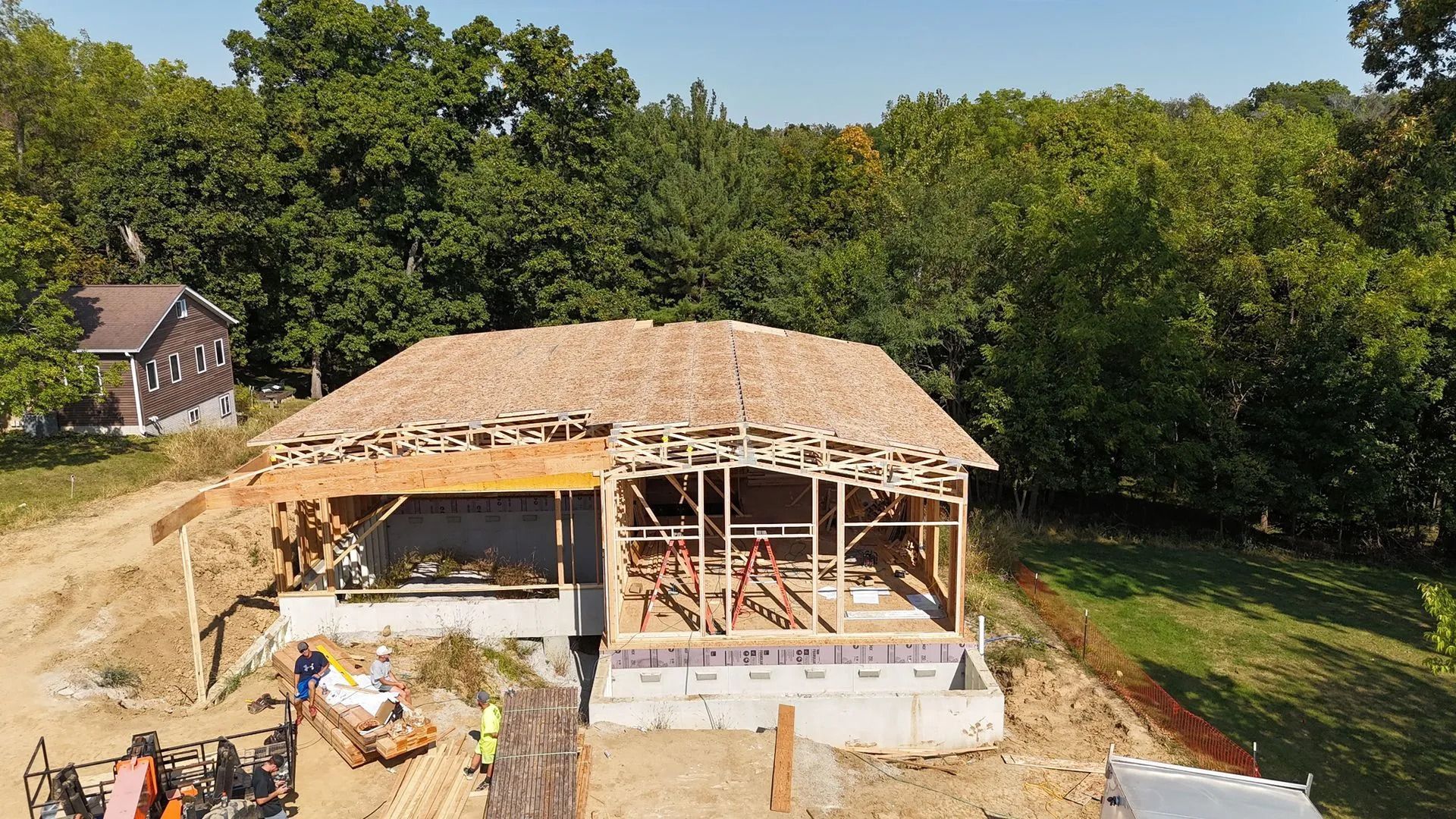 Partially built house with exposed framing and roof under construction in a wooded area
