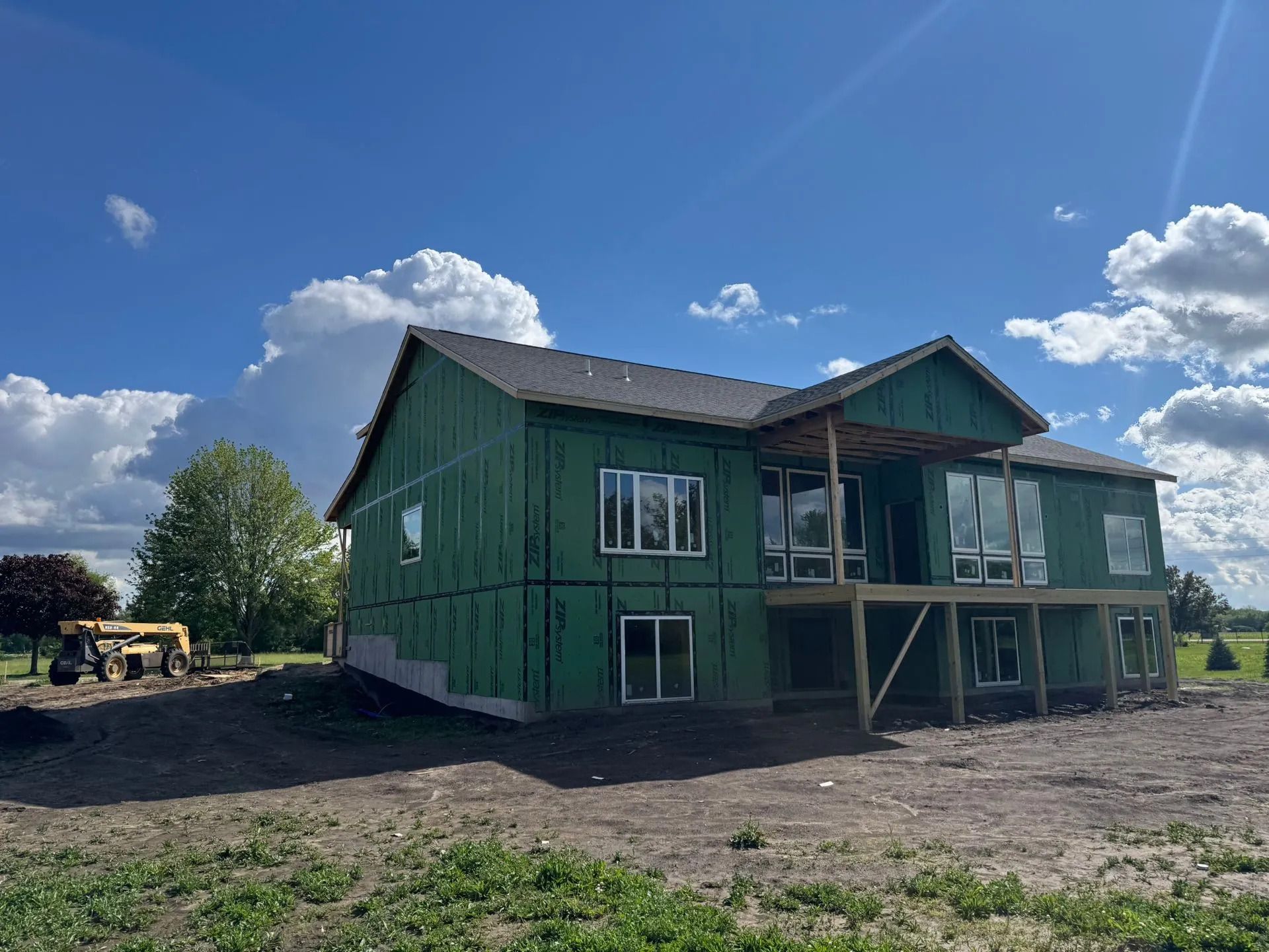 Green house under construction on a dirt lot with a blue sky and clouds overhead