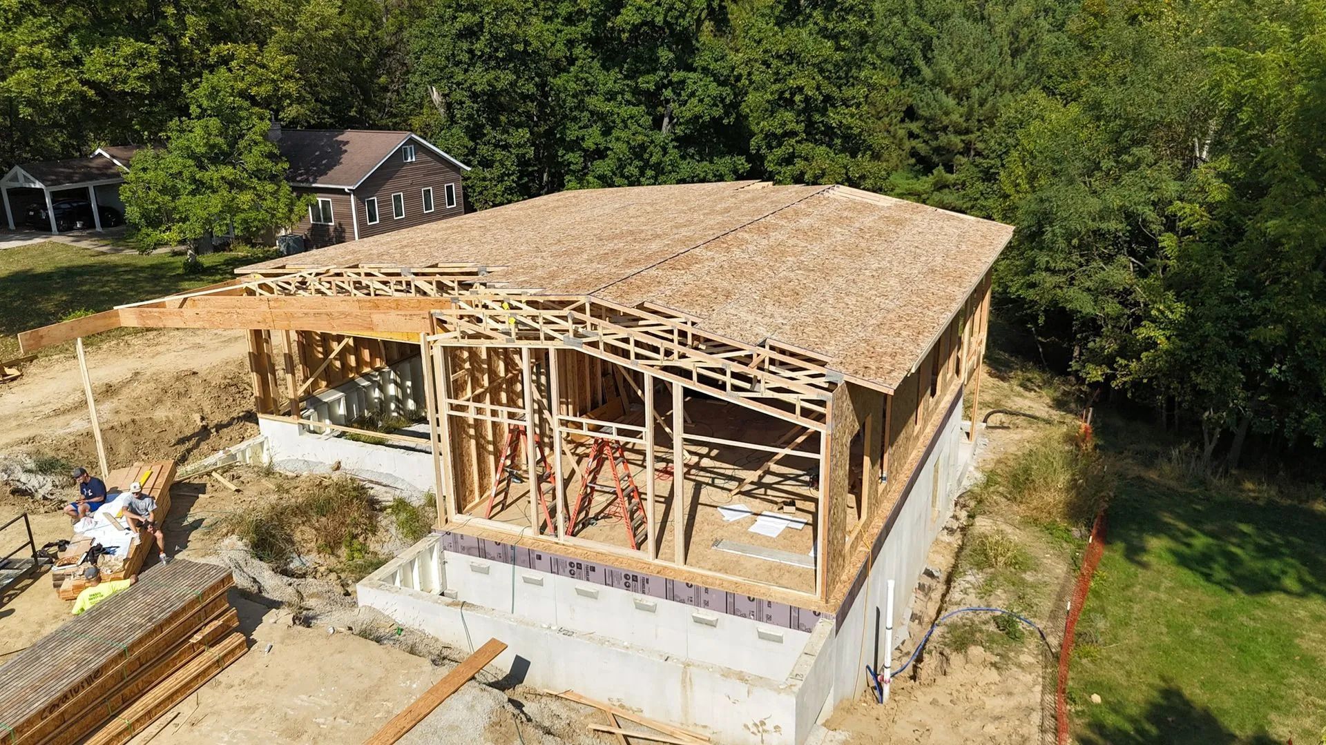 Partially framed house under construction with exposed roof trusses and a concrete foundation