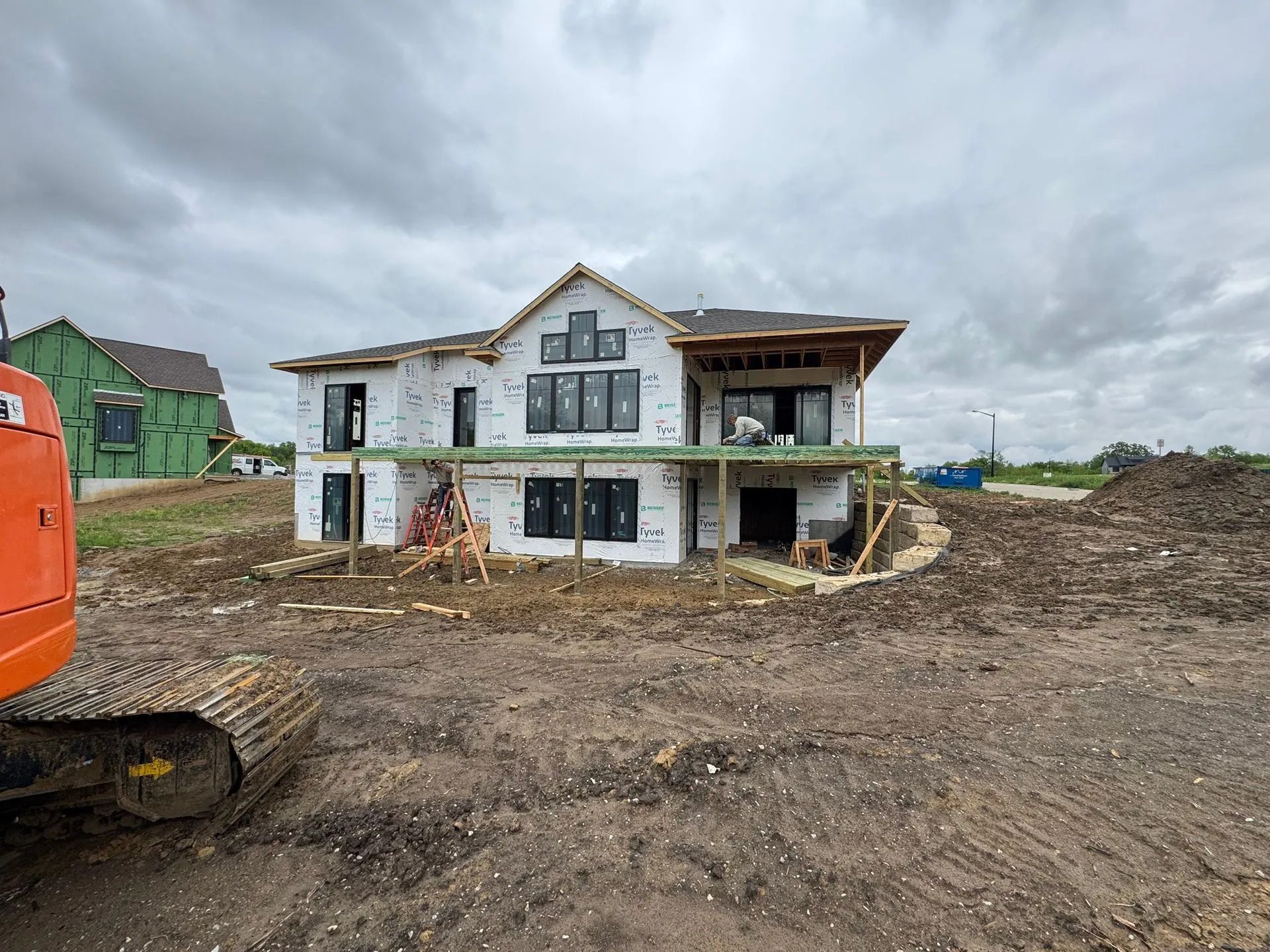 Partially built two-story house on a muddy construction site under cloudy skies