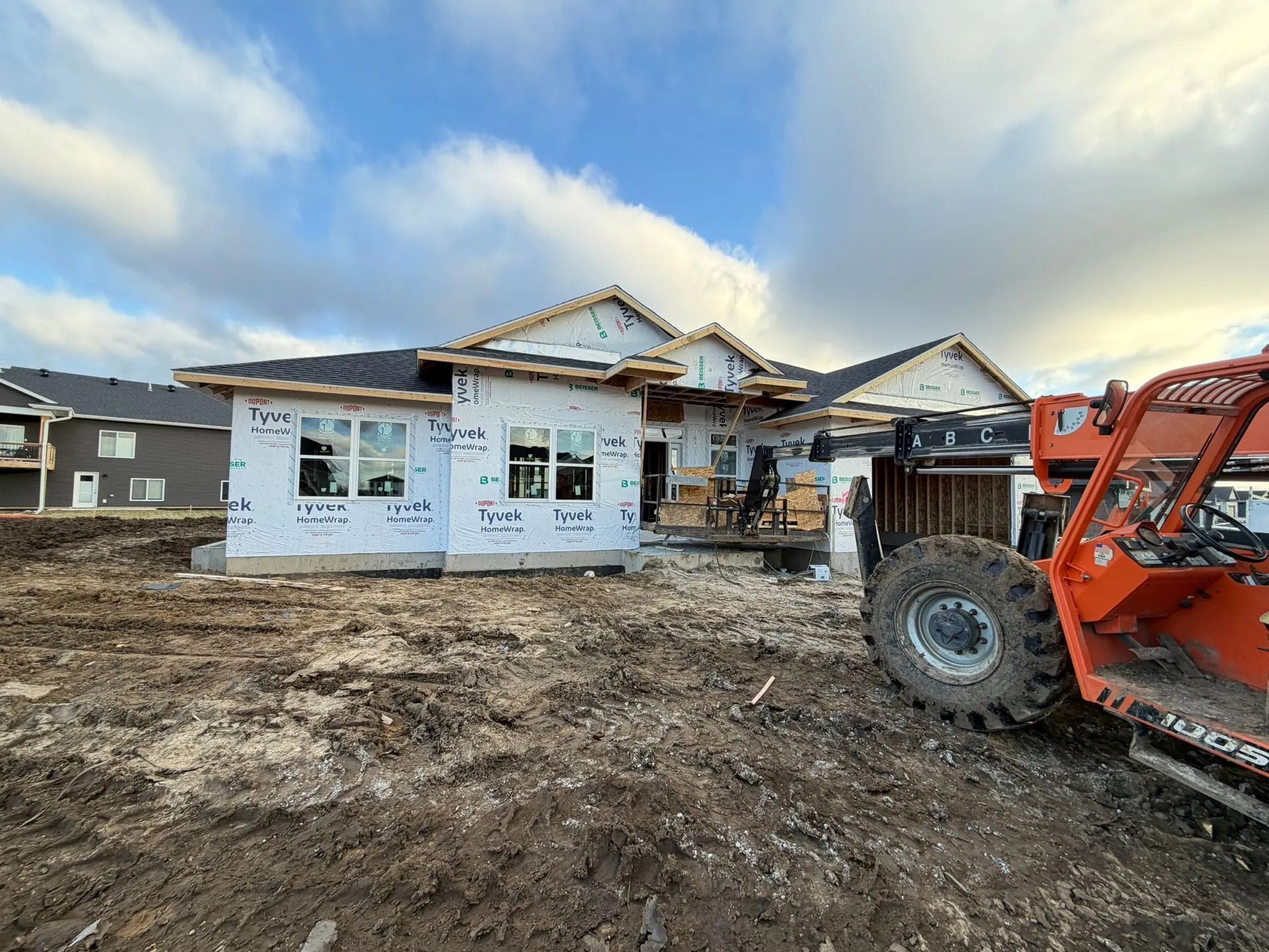 Partially built house under construction with a red skid steer in the foreground