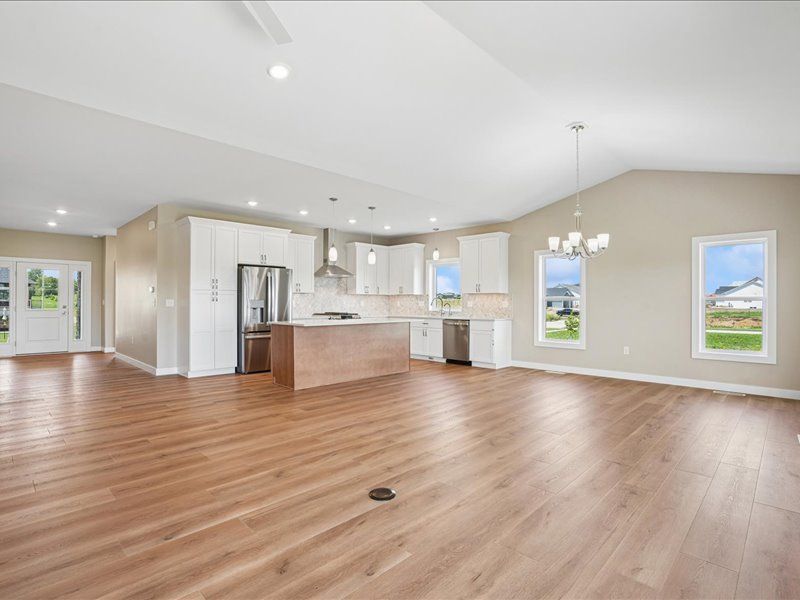 Bright open kitchen and living area with wood floors, white cabinets, stainless fridge, and large windows
