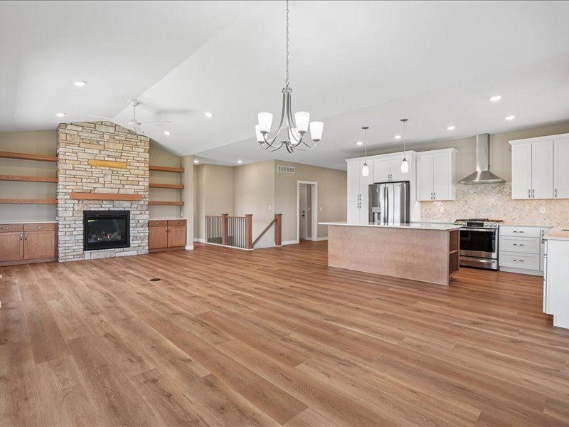 Open-concept living room and kitchen with hardwood floors, stone fireplace, and white cabinetry