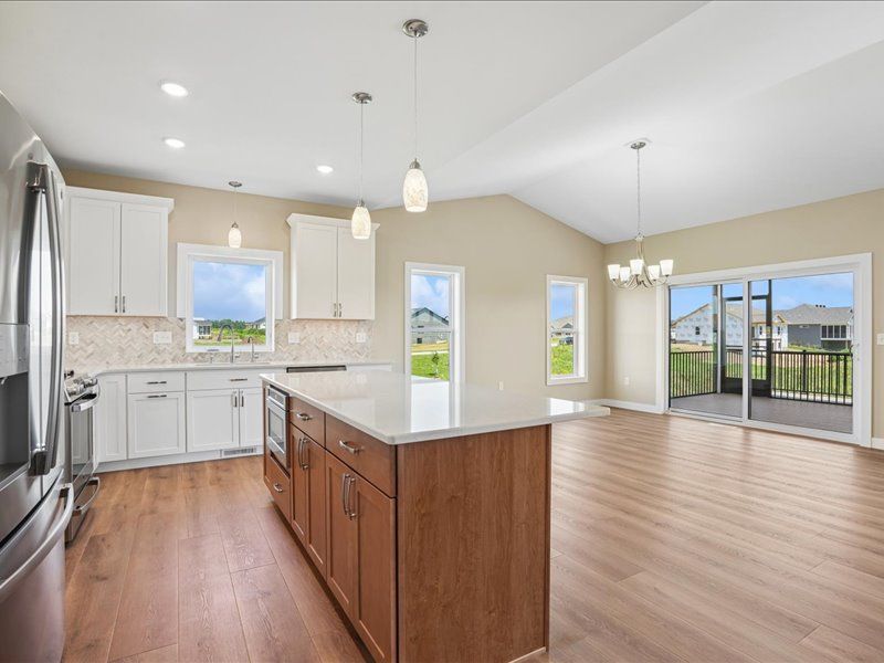 Bright open kitchen and dining area with wood floors, island, white cabinets, and large windows to a deck