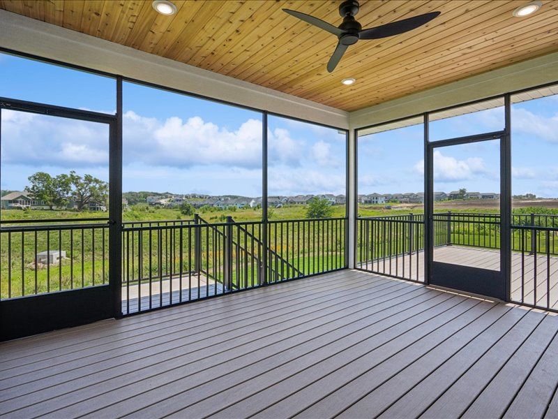 Screened porch with wood ceiling and ceiling fan, overlooking green fields and sky.