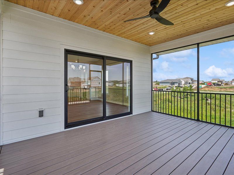 Covered deck with gray flooring, wood ceiling, black railing, and sliding glass doors overlooking a grassy neighborhood.