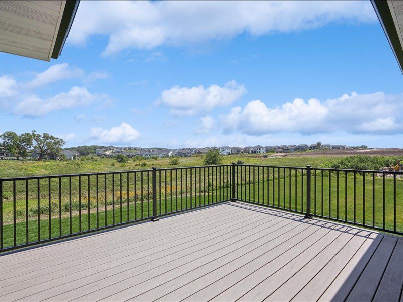 Covered deck overlooking a green field and distant houses under a blue sky