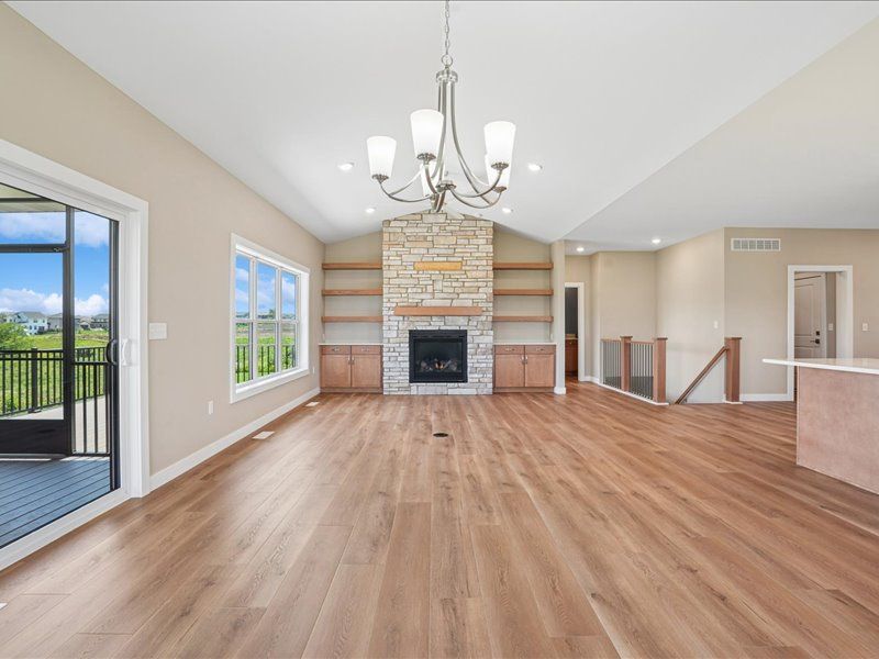 Spacious living room with hardwood floors, chandelier, and stone fireplace, open to a balcony and stairway.