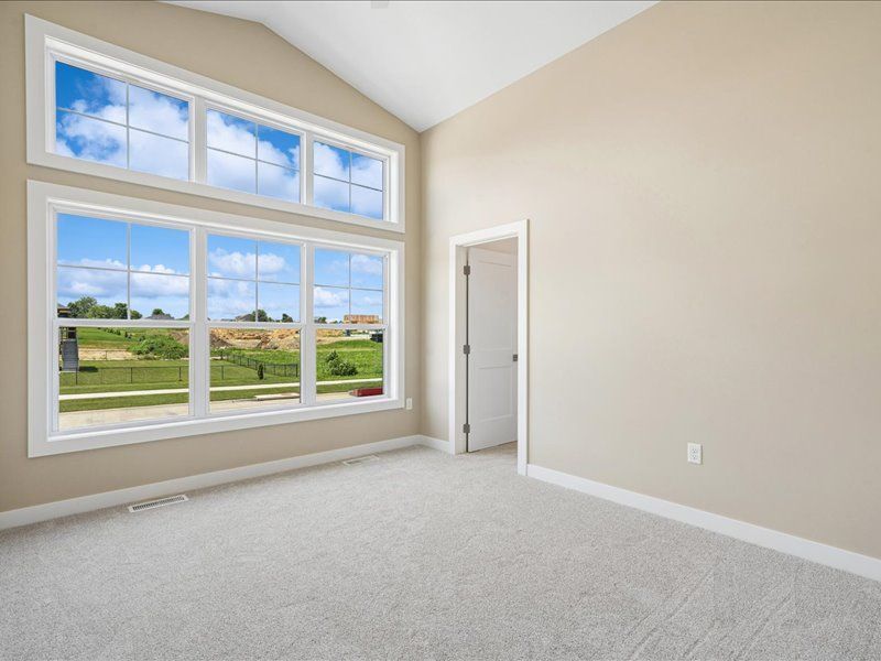 Empty beige room with large windows overlooking a grassy landscape