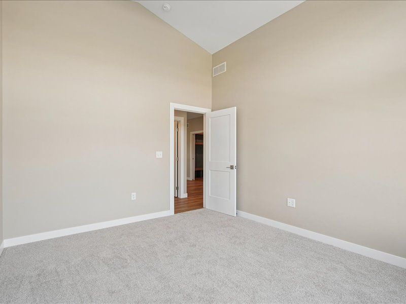 Empty beige bedroom with light carpet and an open doorway to a hallway
