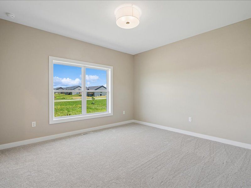 Empty beige bedroom with carpet, window view of houses and mountains, and a ceiling light