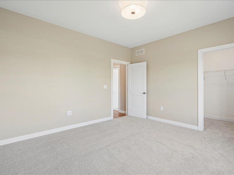 Empty beige bedroom with carpet, white trim, open door, and closet opening
